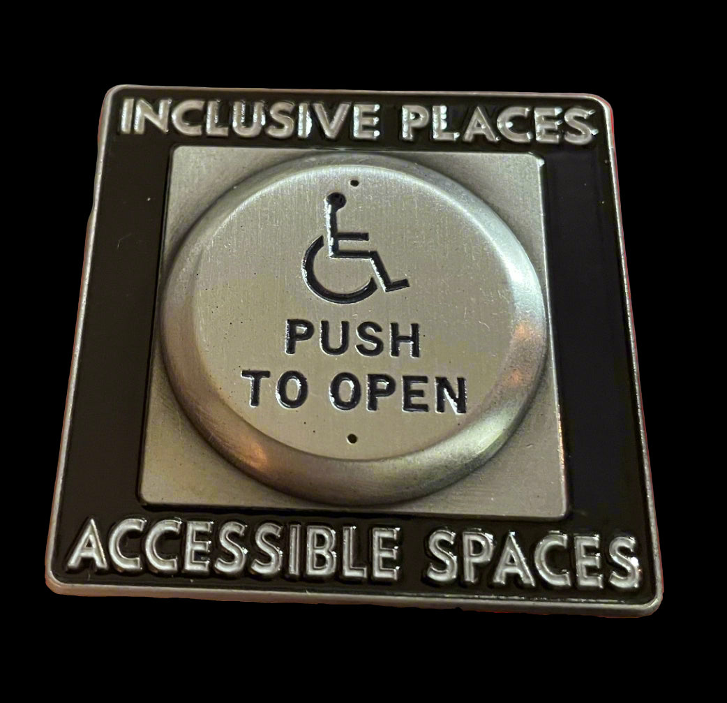 Metallic button with wheelchair icon and text 'Inclusive Places, Push to Open, Accessible Spaces' held in a hand.